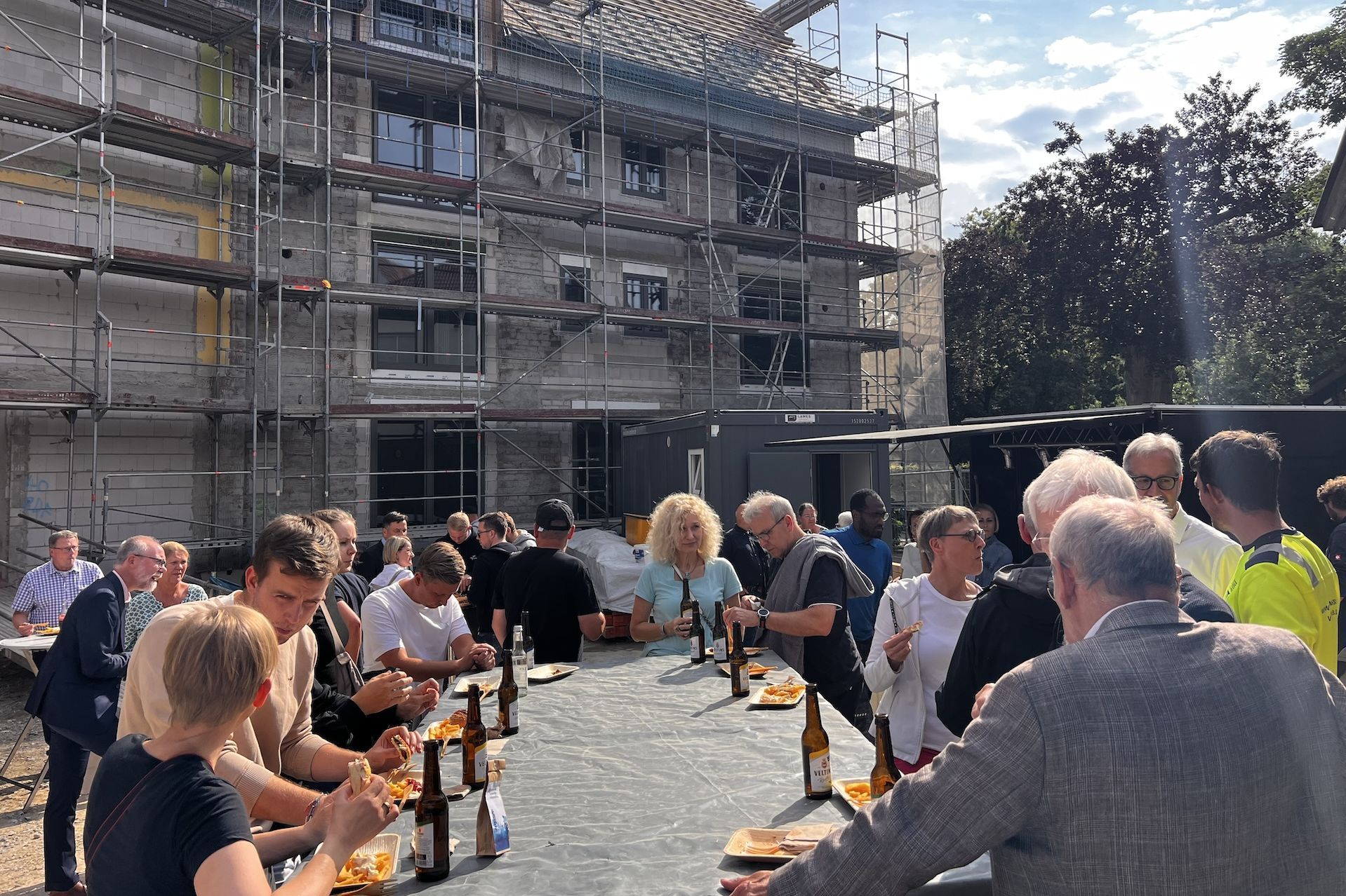Beim Richtfest: Vor dem eingerüsteten Gebäude gibt es in großer Runde Baustellenimbiss: Pommes und Sandwiches.